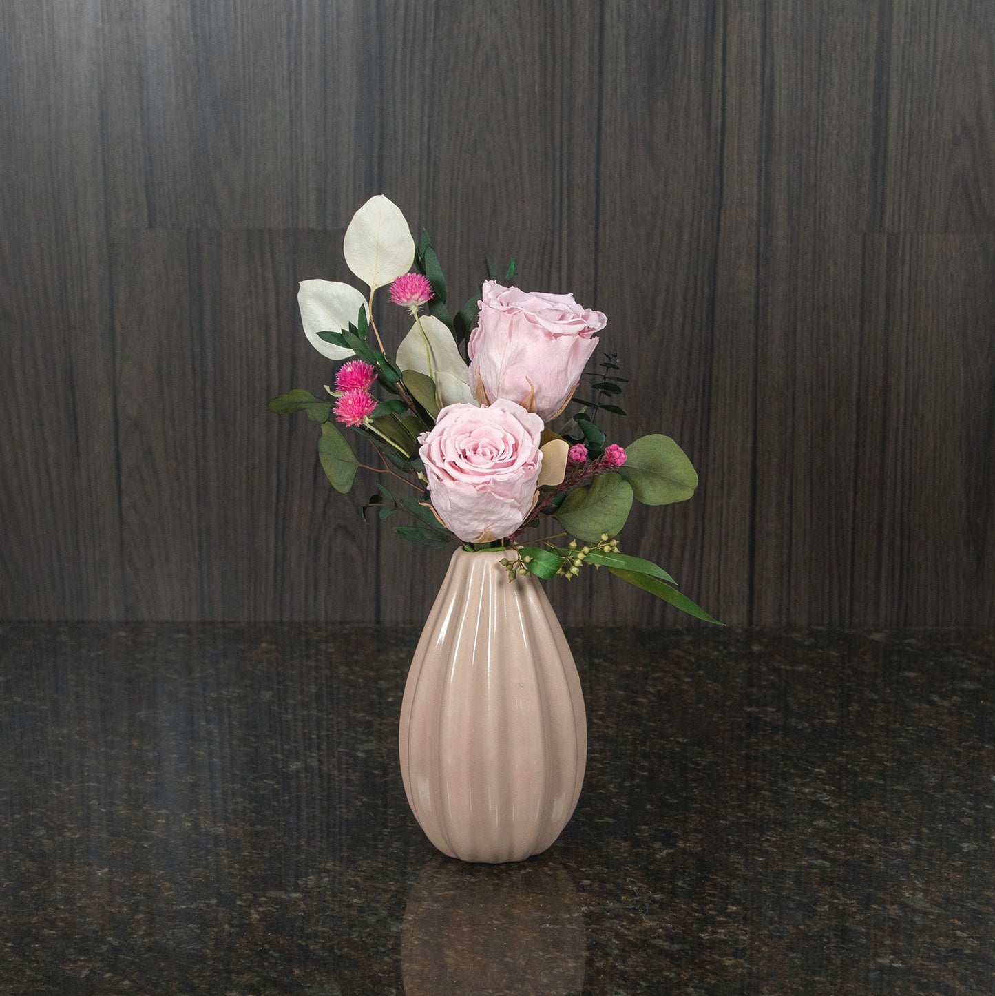 two light pink preserved roses, dried greenery, and dried filler in a mauve pink ceramic bud vase
