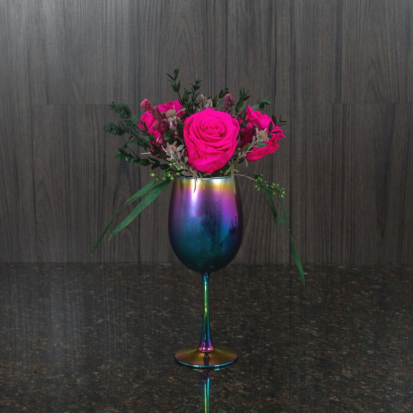 three magenta preserved roses and dried greenery in a colorful metallic stemmed vase