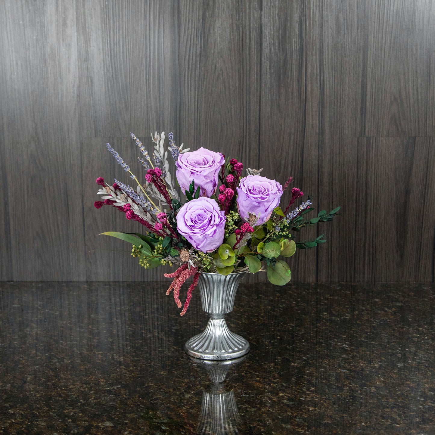 3 lavender preserved roses with dried greenery in a silver metal footed vase