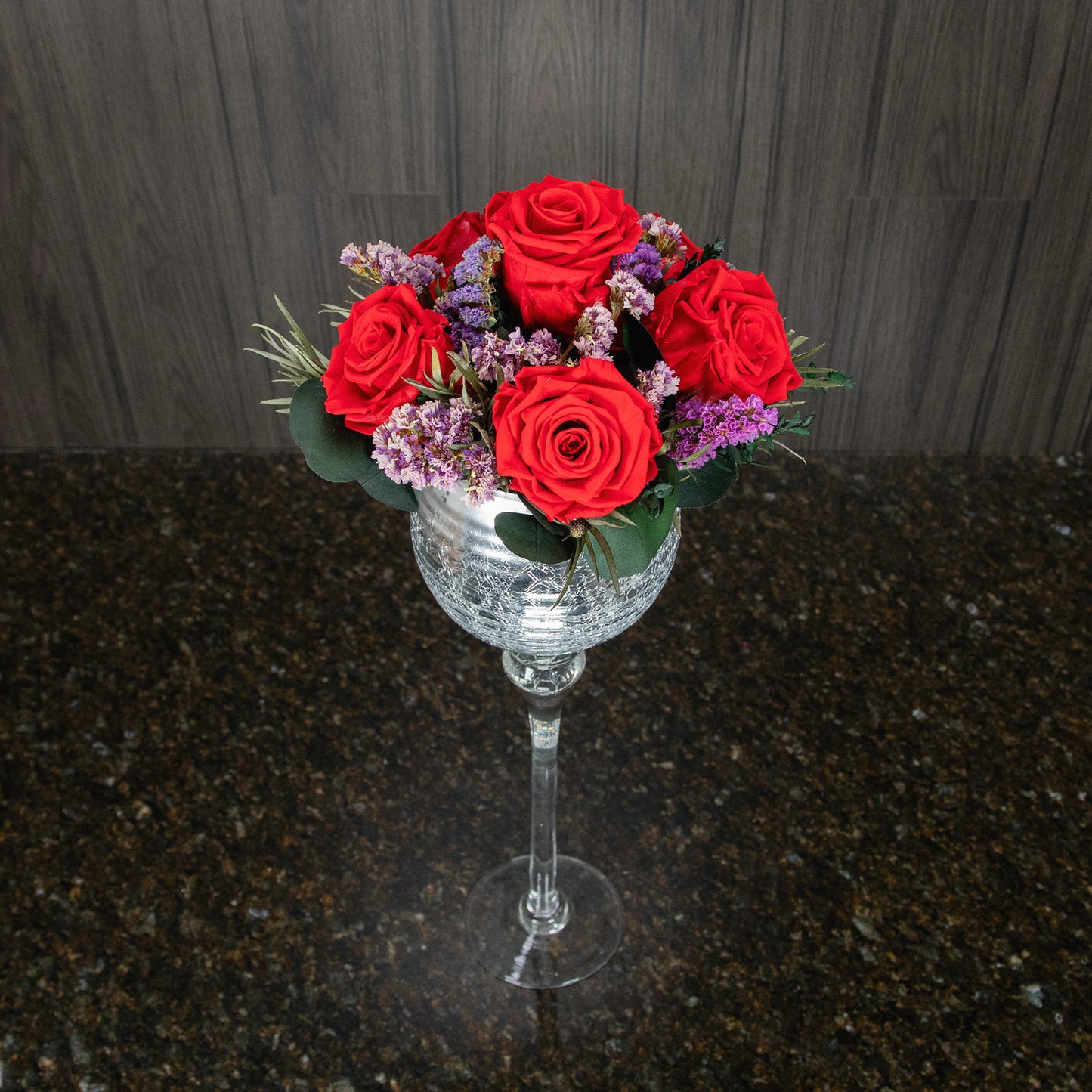 top down view of six preserved red roses, dried greenery, and dried filler flowers in a tall vase