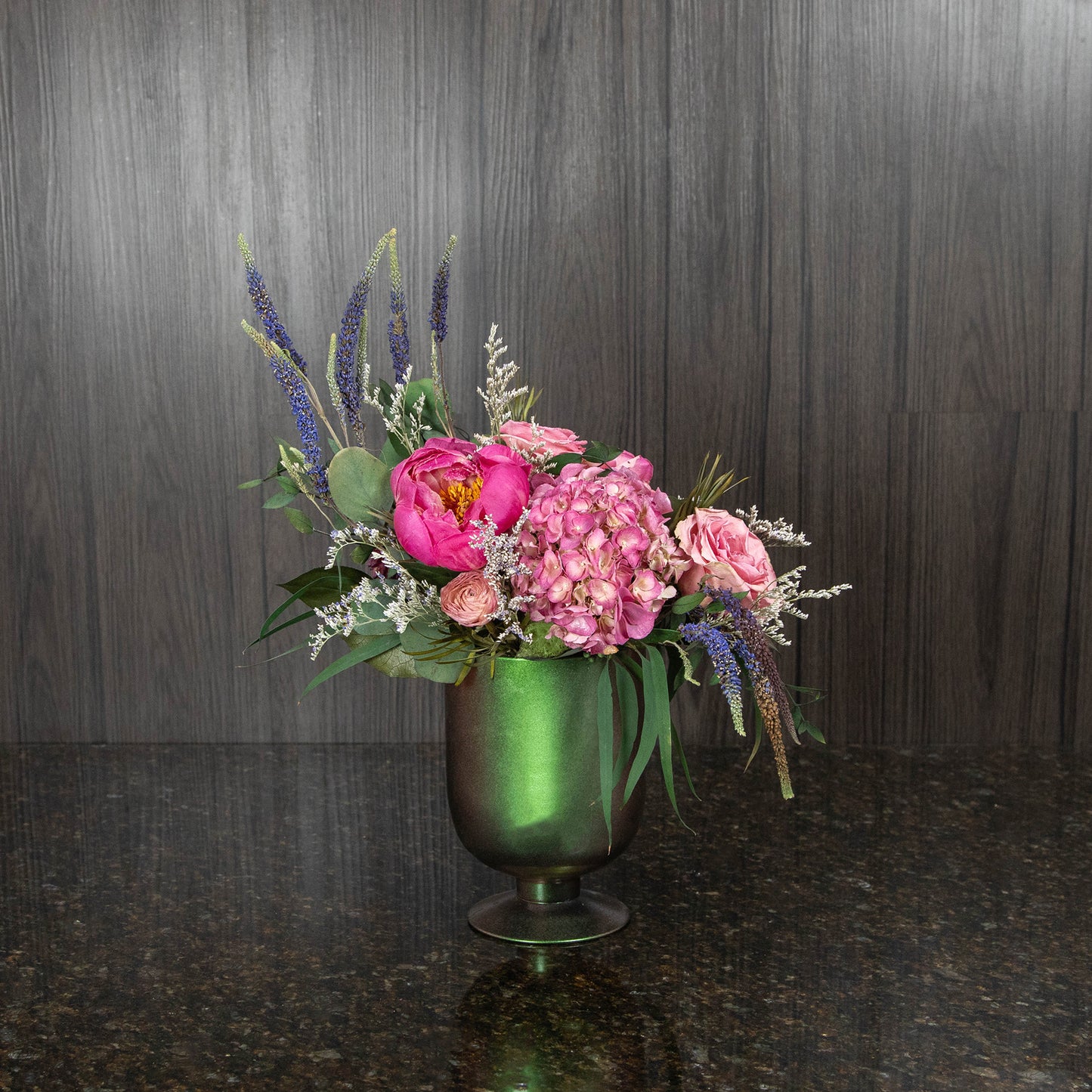 a variety of dried florals and greenery arranged in a metallic green footed vase