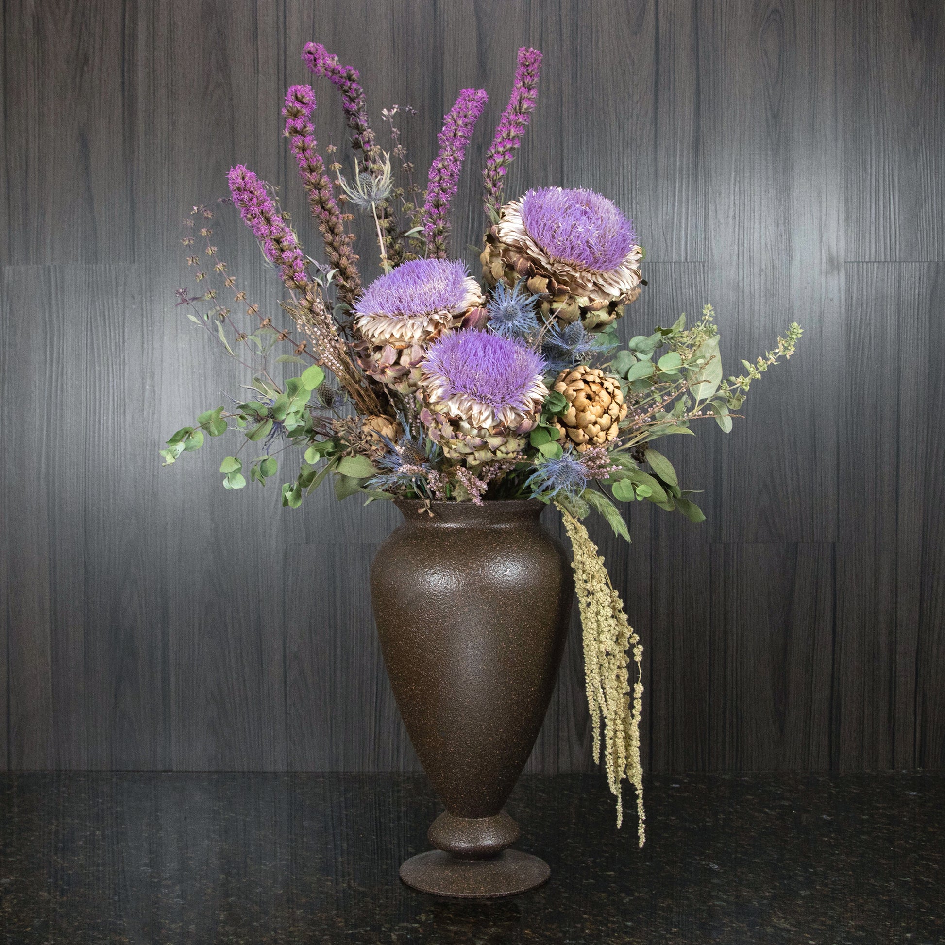 dried artichoke blooms and other dried flowers and greenery in a footed vase