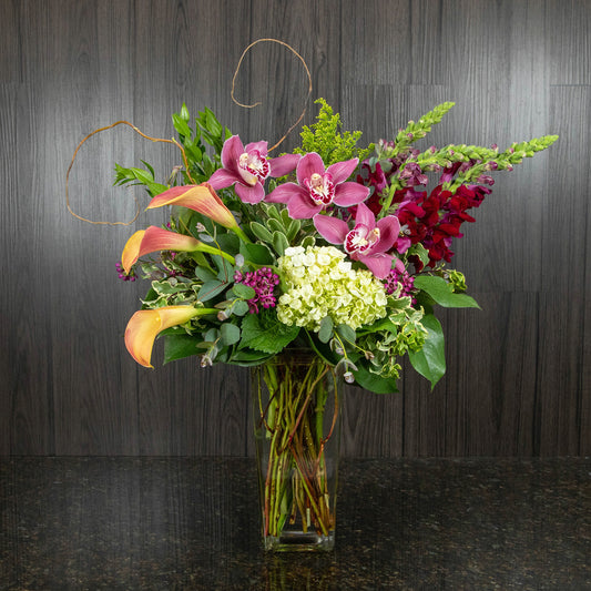 a flower arrangement with summer colors in a tall glass vase