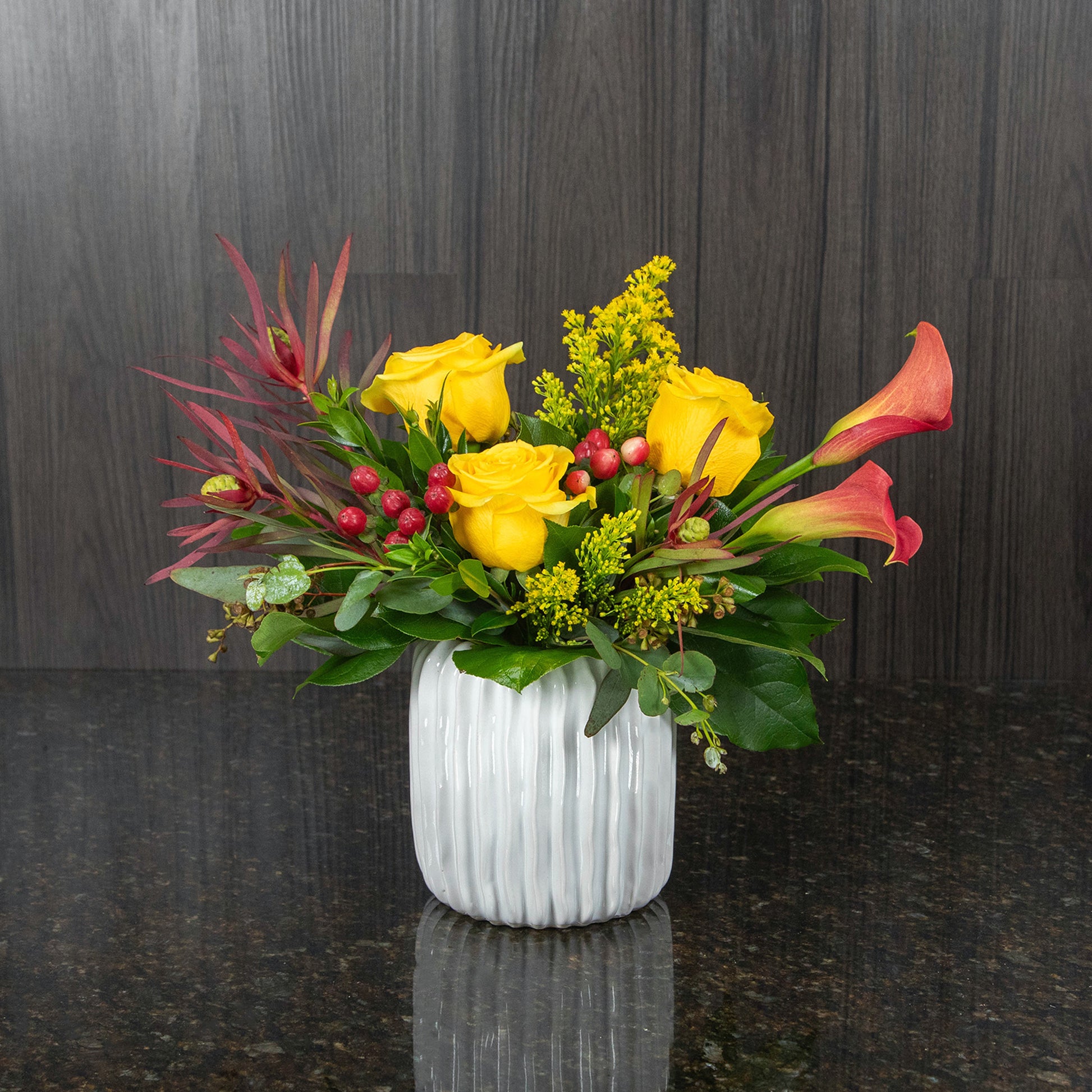 a flower arrangement in shades of yellow, red, and orange in a textured white pot