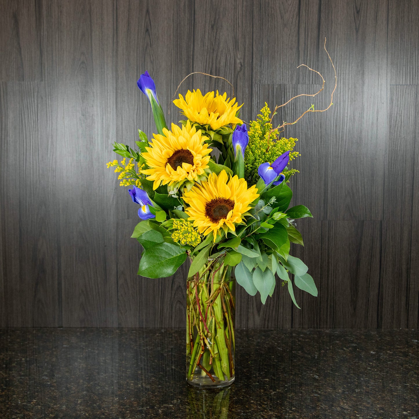 a tall flower arrangement featuring yellow sunflowers and blue irises