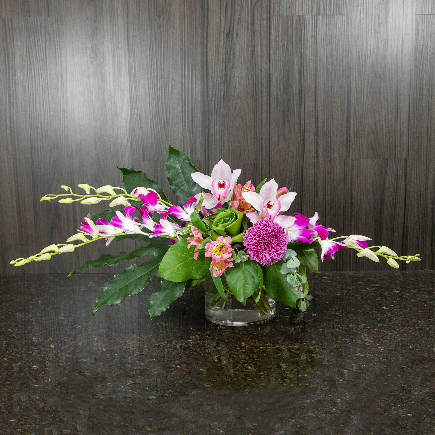 a flower arrangement in a cylinder glass vase with purple dendrobium orchids on each side