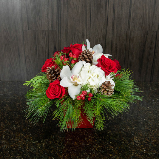 a compact flower arrangement with red and white flowers and pine greenery